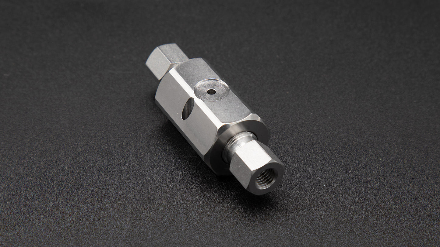 A small metal valve resting on a smooth black surface, showcasing its metallic sheen and intricate design.