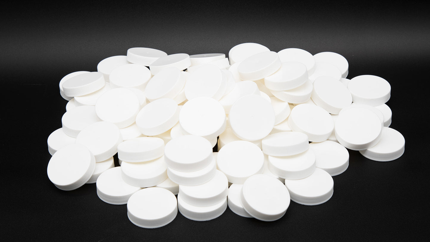 A close-up of a pile of white plastic round bottle caps arranged on a smooth black surface, creating a striking contrast.