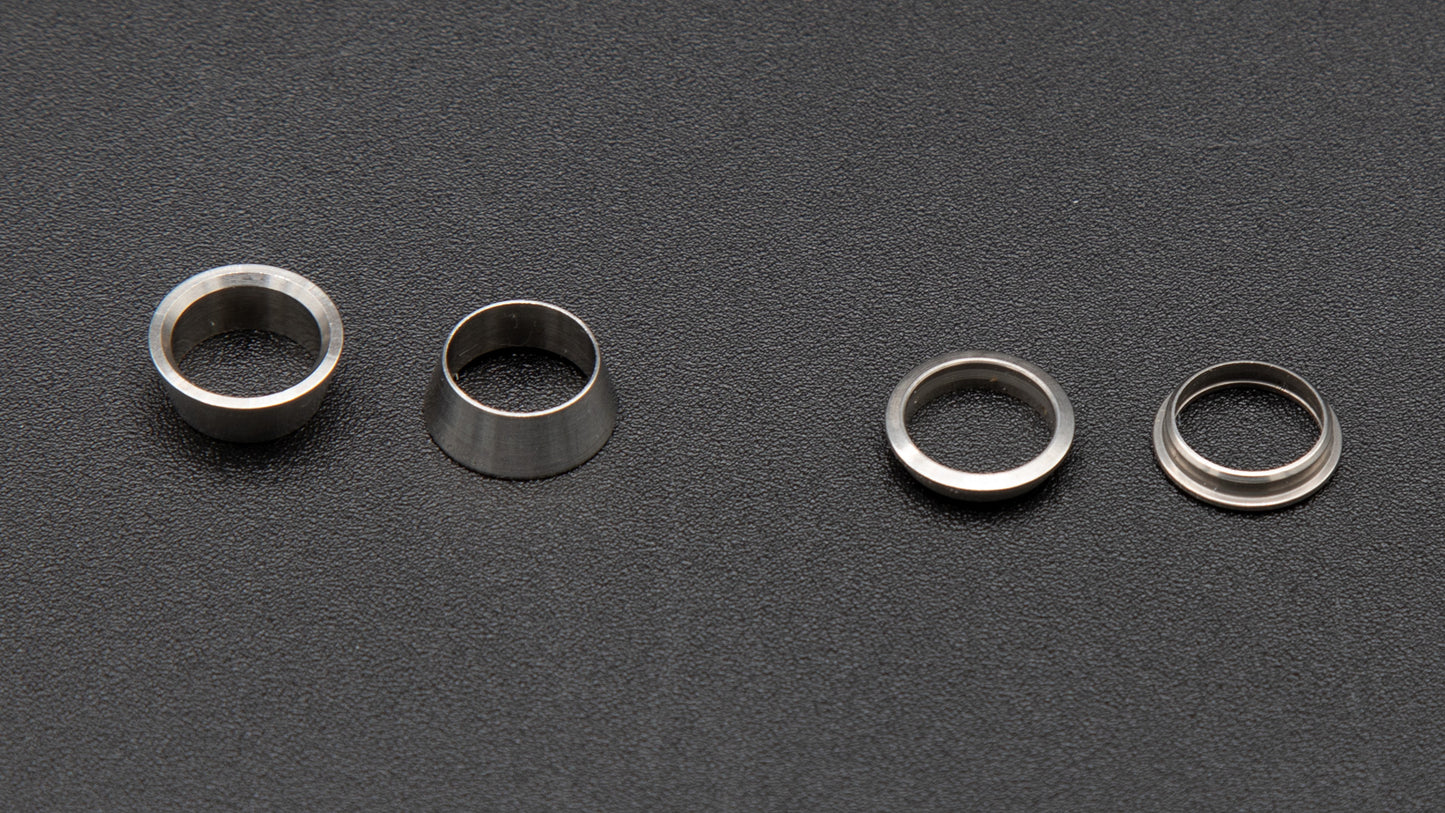 Four silver metal rings arranged on a smooth black surface, showcasing their reflective surfaces and circular design.