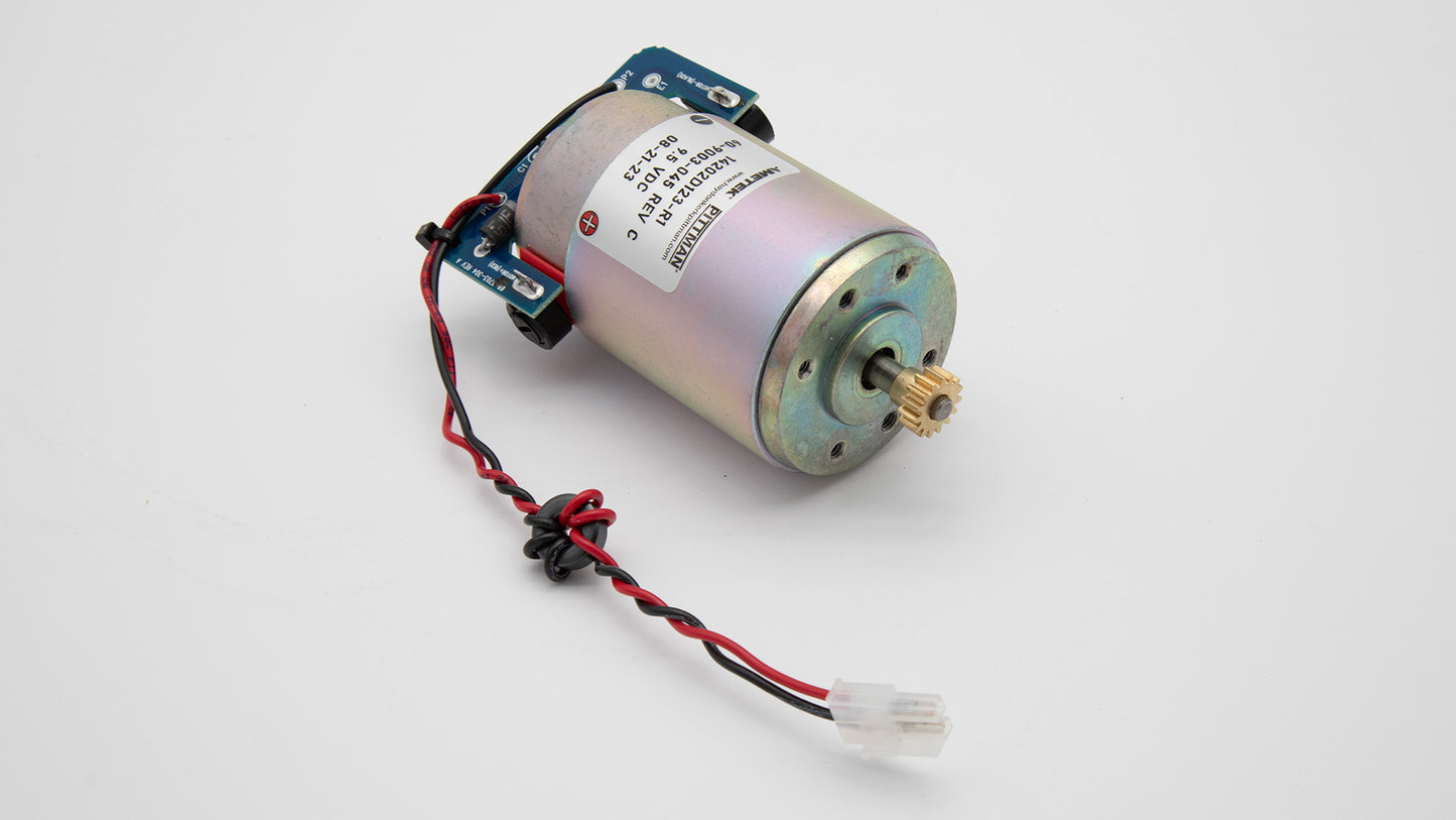 A small motor with visible wires resting on a white surface, emphasizing its size and electrical connections.