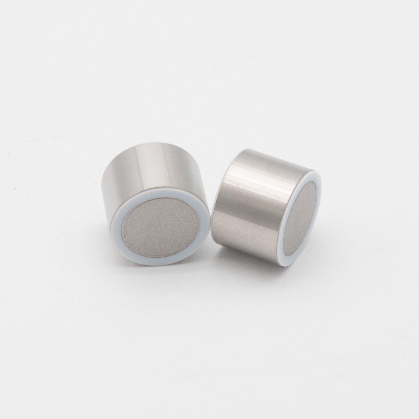 Two silver metal cylinders placed on a clean white surface, showcasing their reflective surfaces and sleek design.