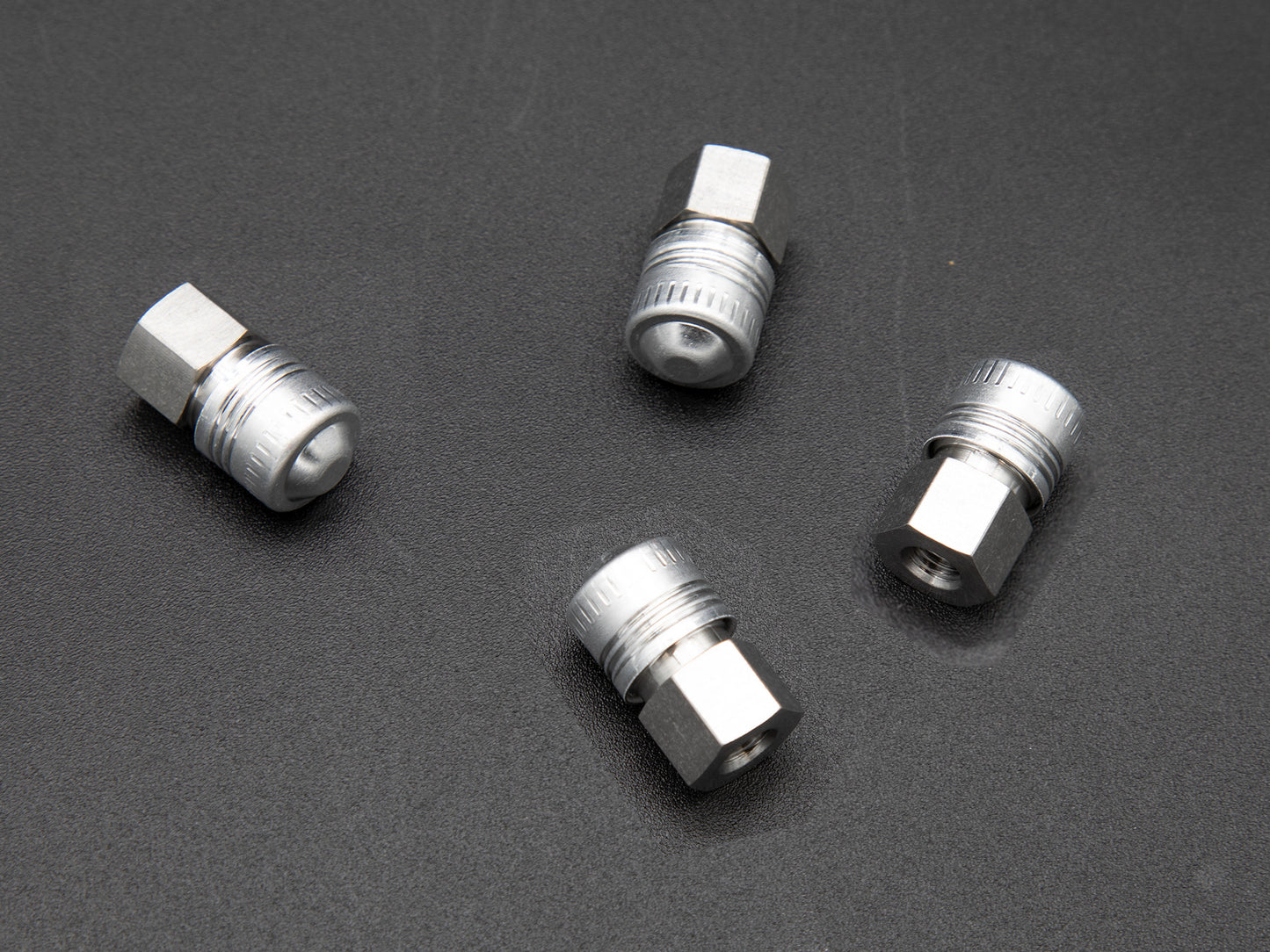Four silver metal threaded fittings arranged neatly on a smooth black surface, showcasing their metallic sheen and design.