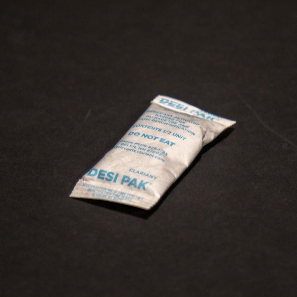 A small white bag of desiccant resting on a sleek black surface.