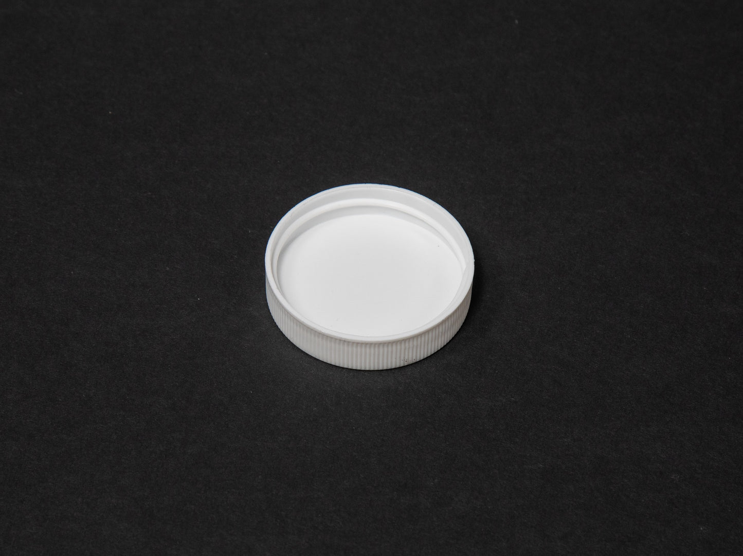 A white plastic bottle cap situated on a black surface, showcasing a striking visual contrast between the two elements.