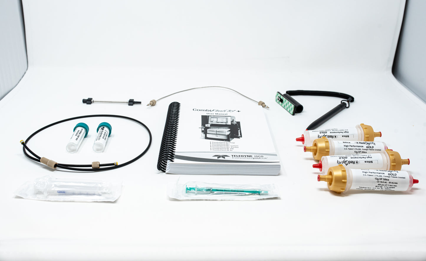 A collection of components featuring a notebook, columns with gold caps, tubing, syringes and stylus pen arranged together.