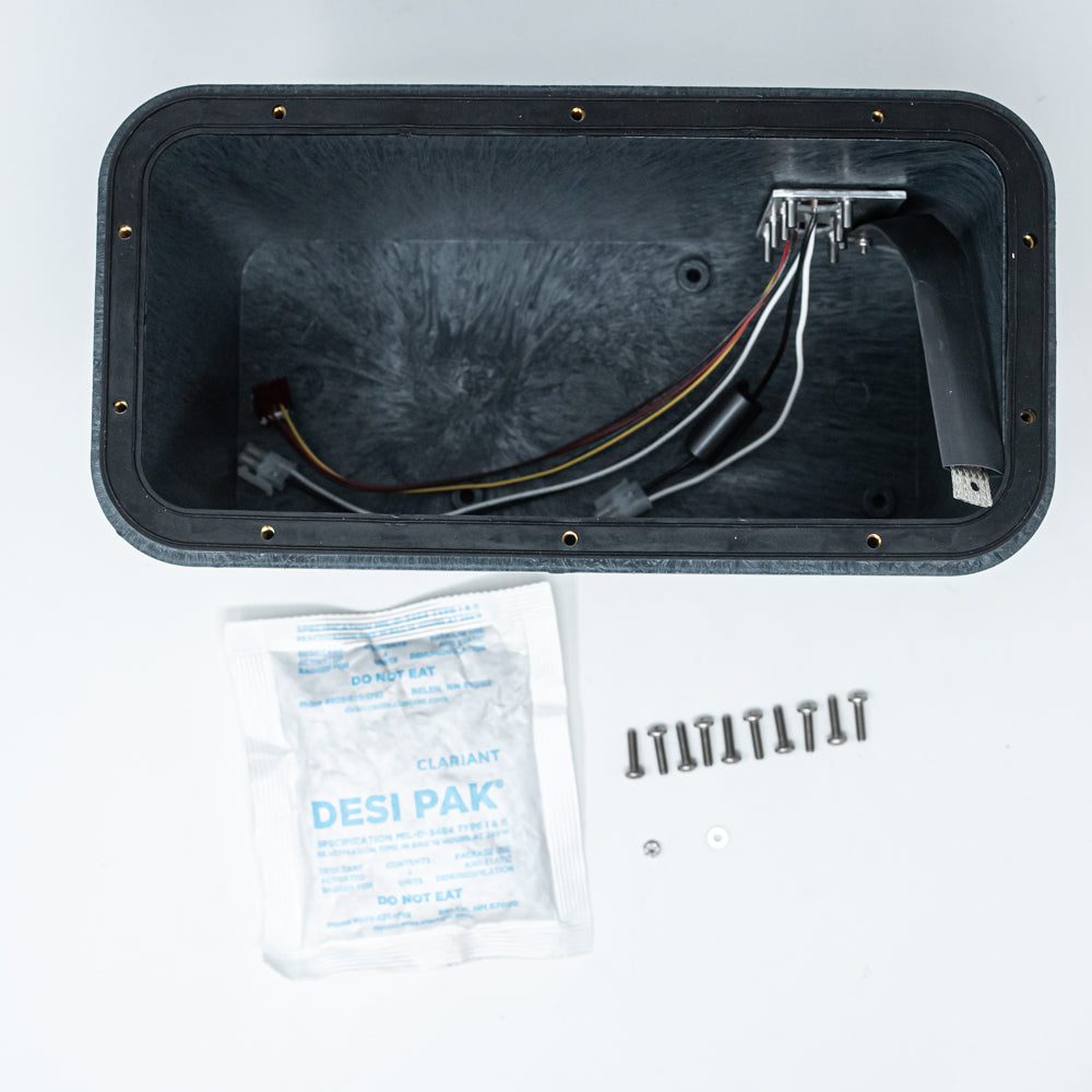 A black box with multiple wires attached, next to a desiccant bag, representing a configuration of electronic devices.