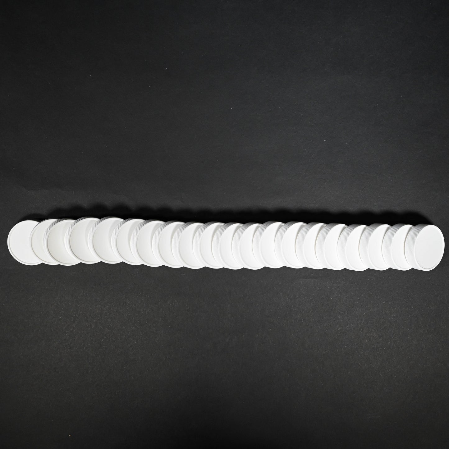 A linear arrangement of white bottle caps positioned on a black background, emphasizing the simplicity and elegance of the design.