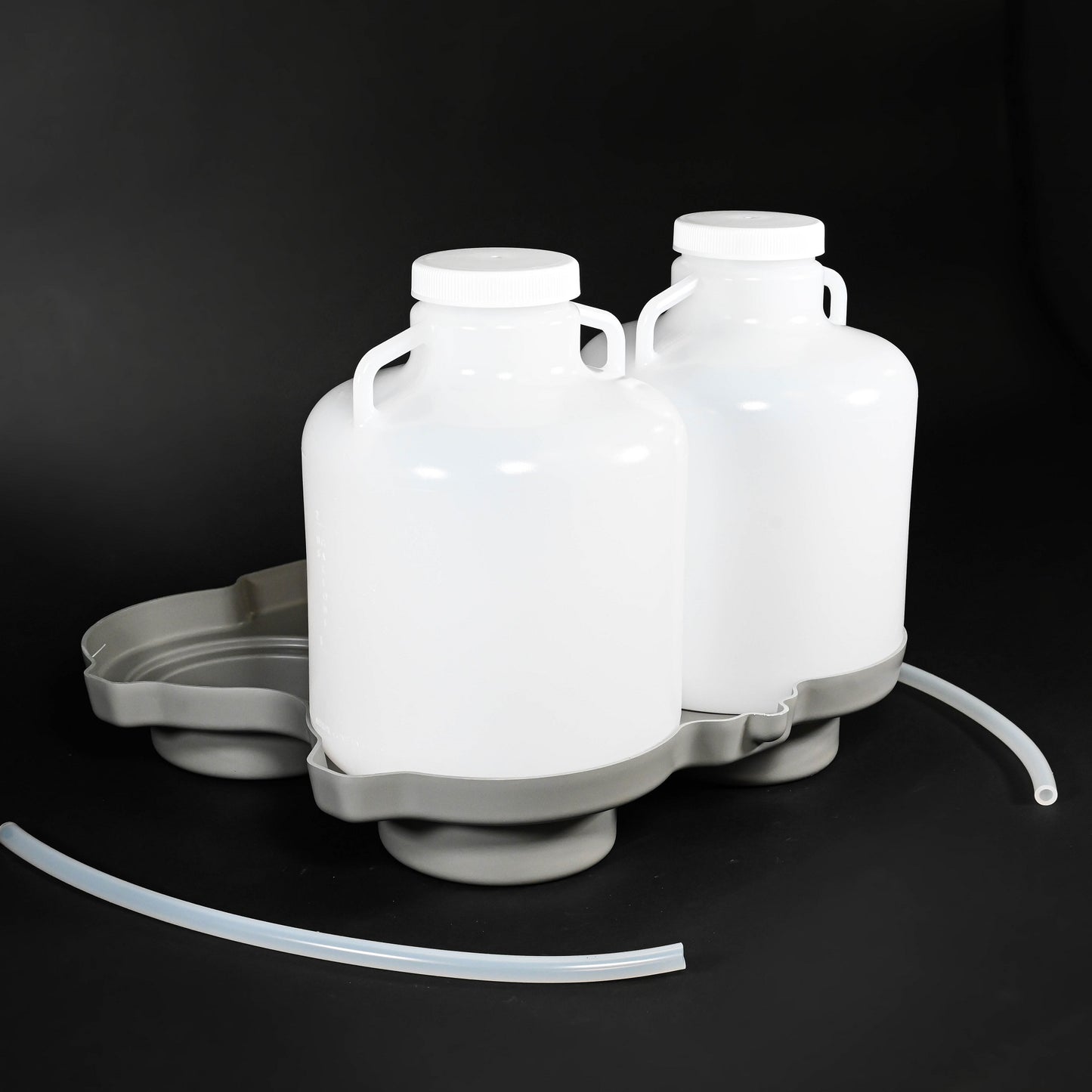 Two plastic bottles with lids placed on a grey locating base, accompanied by a handle and two tubes, arranged neatly on a surface.