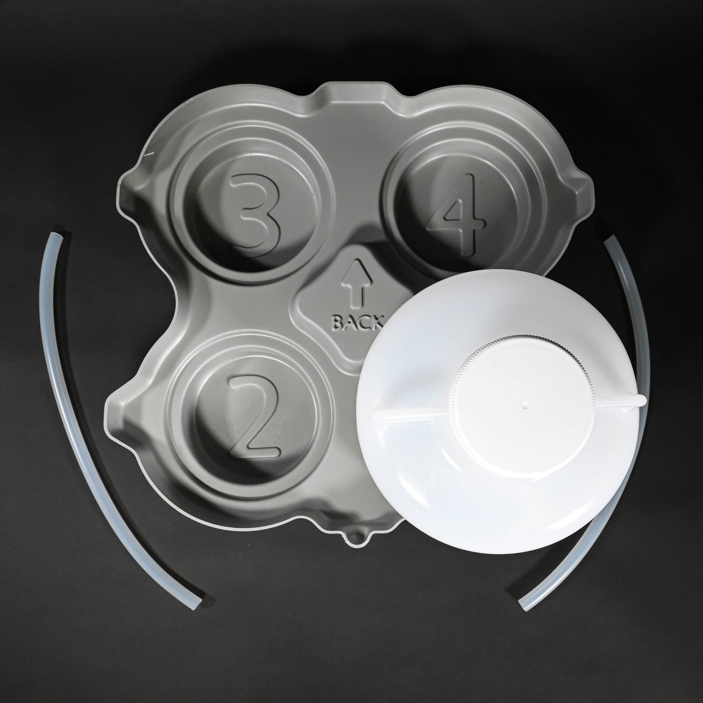 A plastic bottle with lid placed on a grey locating base, accompanied by a handle and two tubes, arranged neatly on a surface.