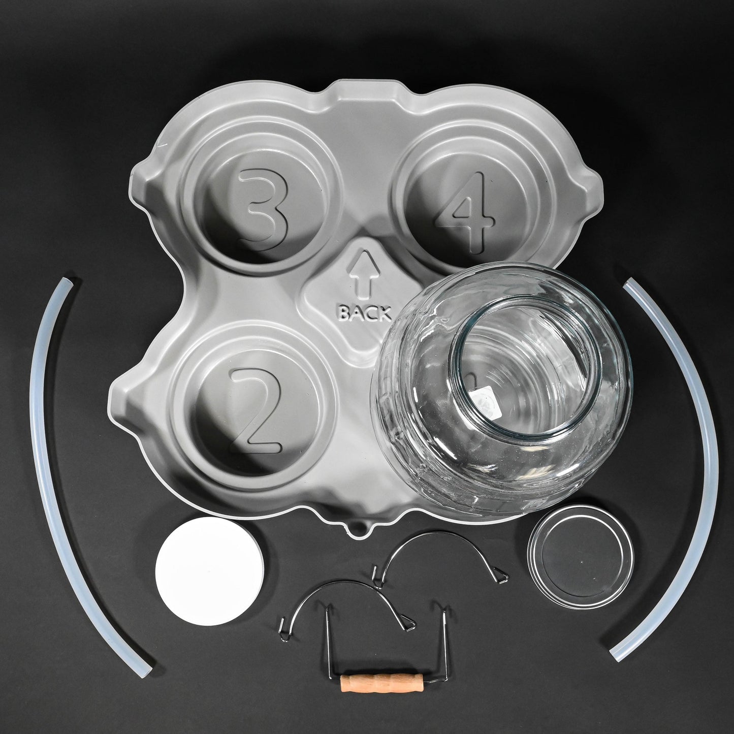 A glass jar with lids placed on a grey locating base, accompanied by a handle and two tubes, arranged neatly on a surface.