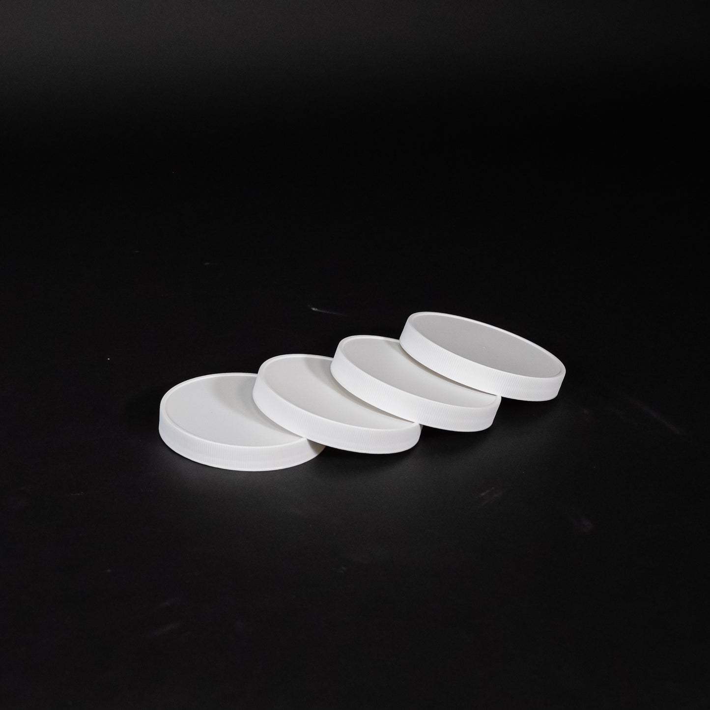 Four white plastic lids arranged on a black surface, showcasing their smooth texture and circular shape.