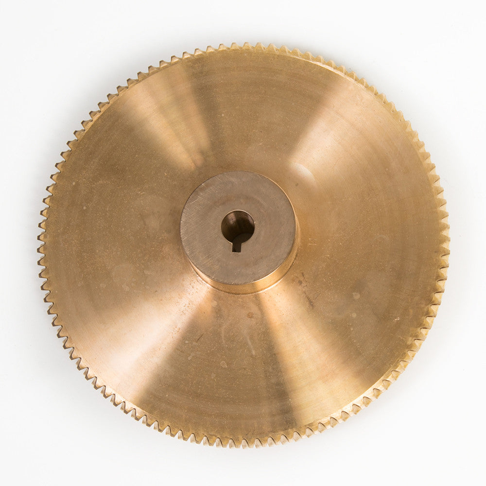 A gold metal gear wheel resting on a clean white surface, showcasing its intricate design and shiny finish.