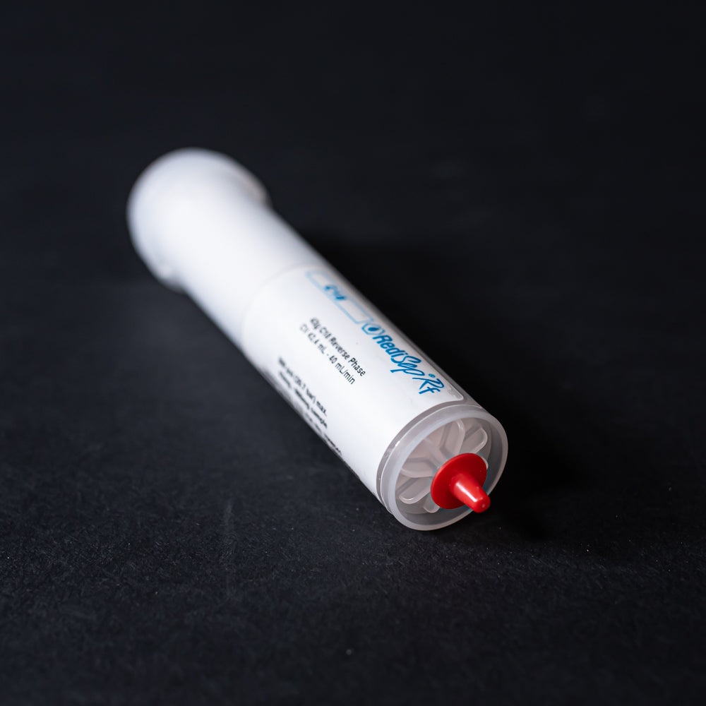A small white tube with red caps displayed on a black background, creating a striking visual contrast between the two elements.
