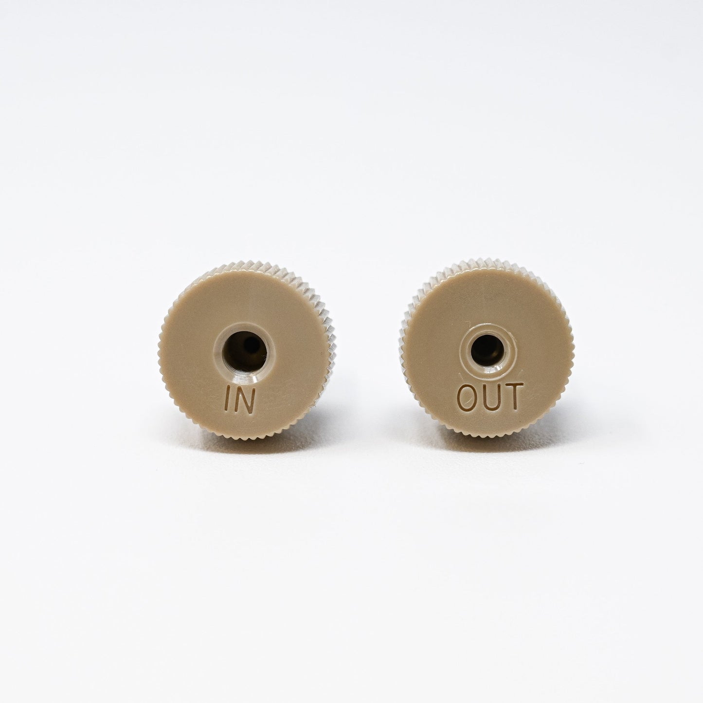 Two tan colored threaded check valves labeled "in" and "out" positioned side by side on a neutral background.