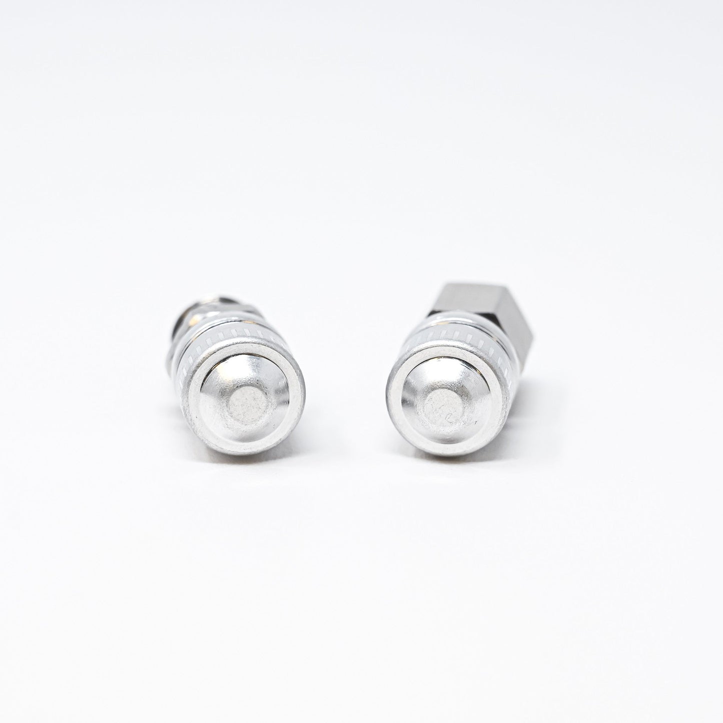 Two silver cylindrical shaped objects placed on a smooth white surface, showcasing their reflective surfaces and circular design.