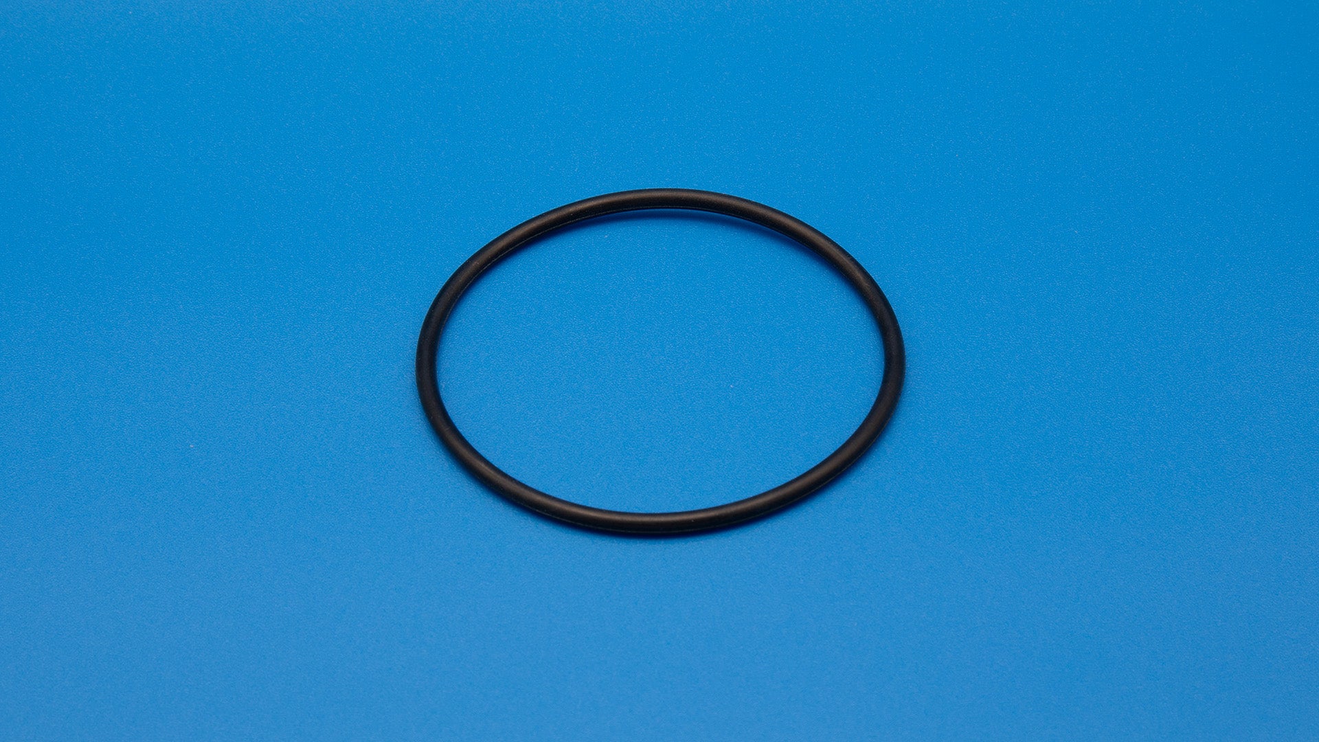 A black rubber O-ring positioned against a vibrant blue background, showcasing its circular shape and texture.