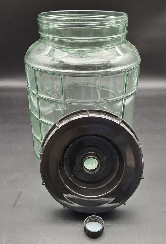 A clear ribbed glass jar with a black screw-on lid and a small detached cap, photographed on a dark gray background.