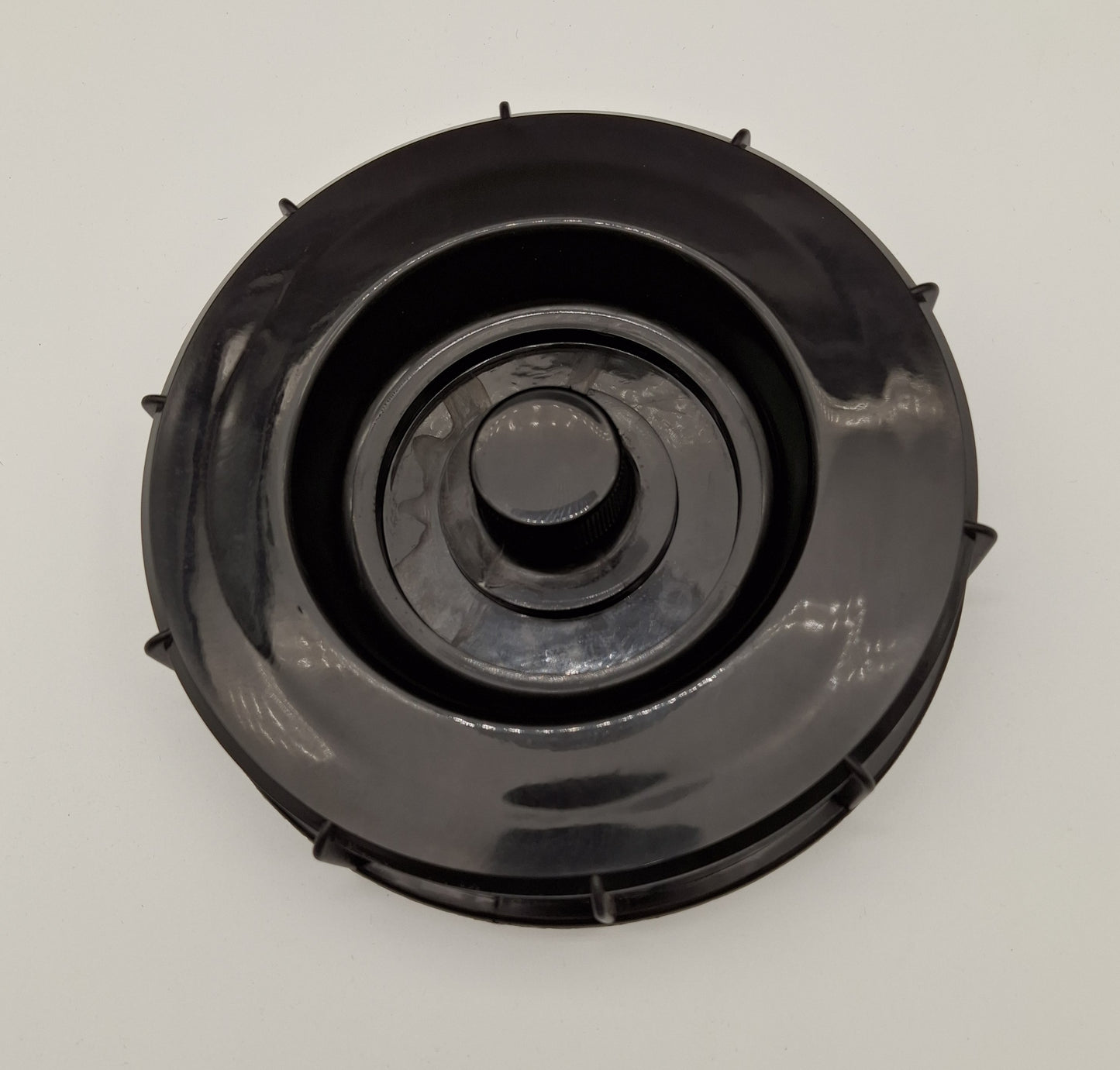 A black circular plastic component, likely a filter cover or cap, photographed from directly above on a light gray background.
