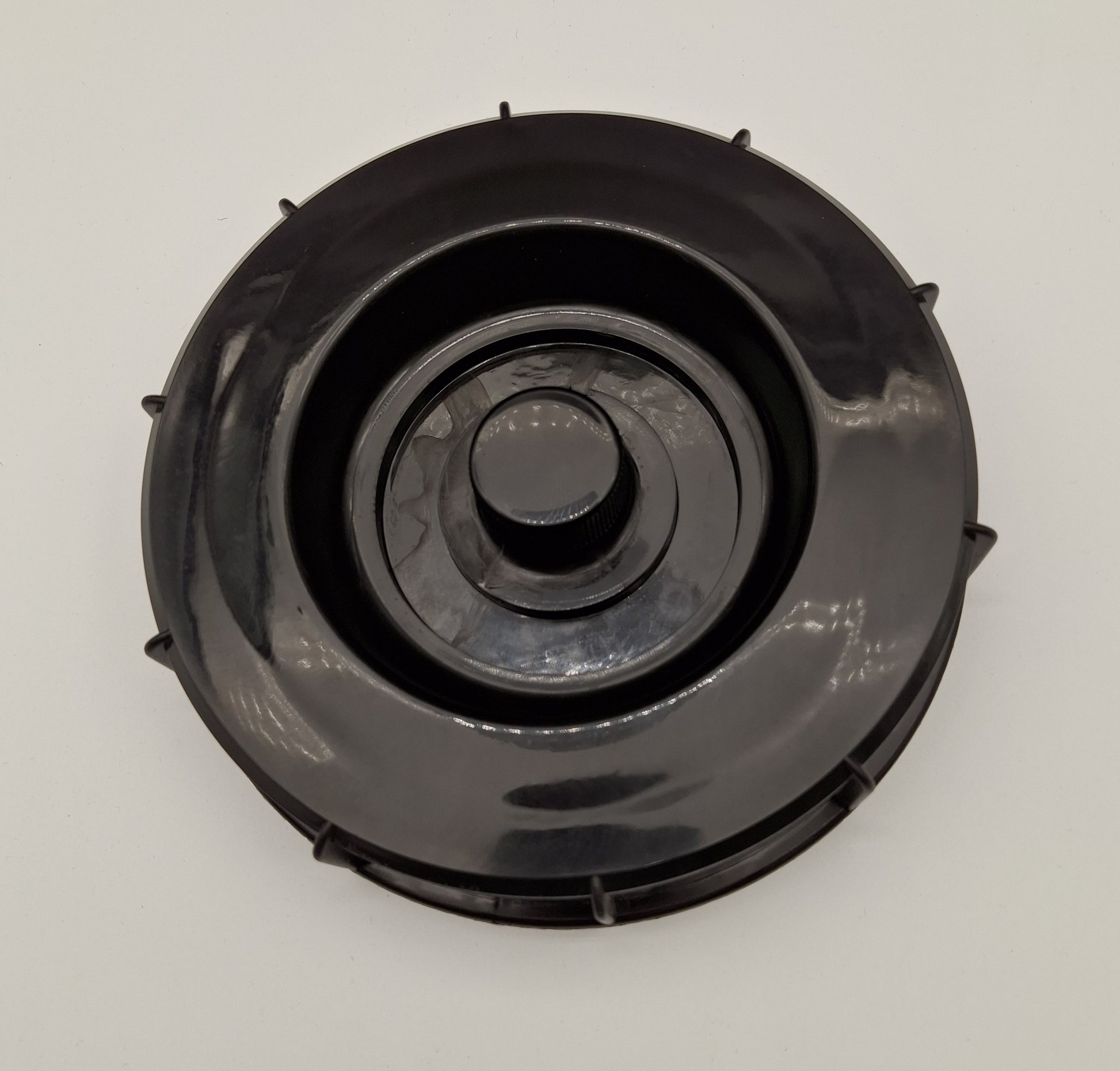 A black circular plastic component, likely a filter cover or cap, photographed from directly above on a light gray background.