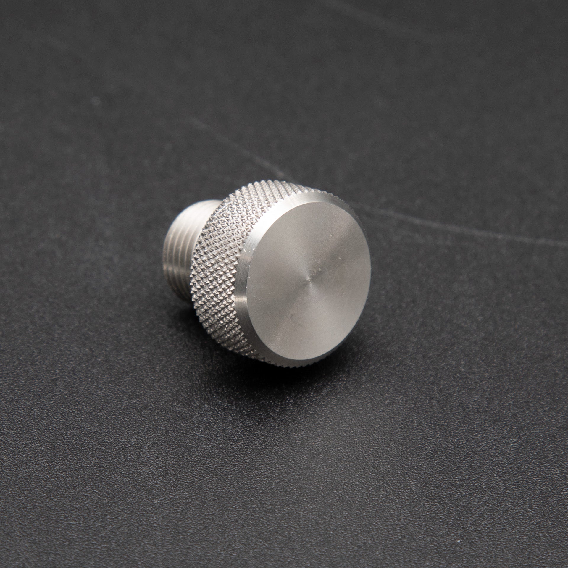 A small metal threaded nut resting on a smooth black surface, showcasing its intricate design and metallic sheen.