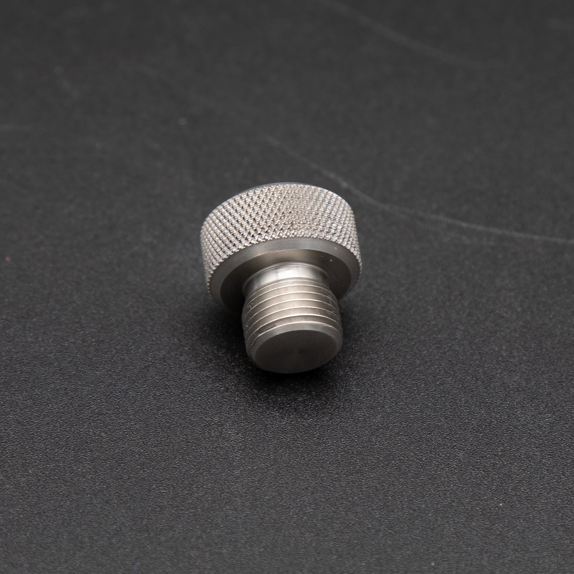 A small metal threaded nut resting on a smooth black surface, showcasing its intricate design and metallic sheen.