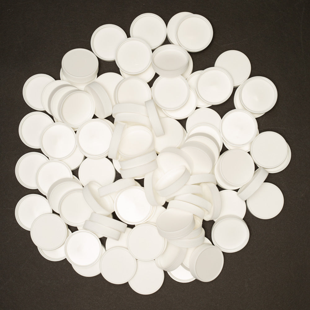 A close-up of a pile of white plastic round bottle caps arranged on a smooth black surface, creating a striking contrast.