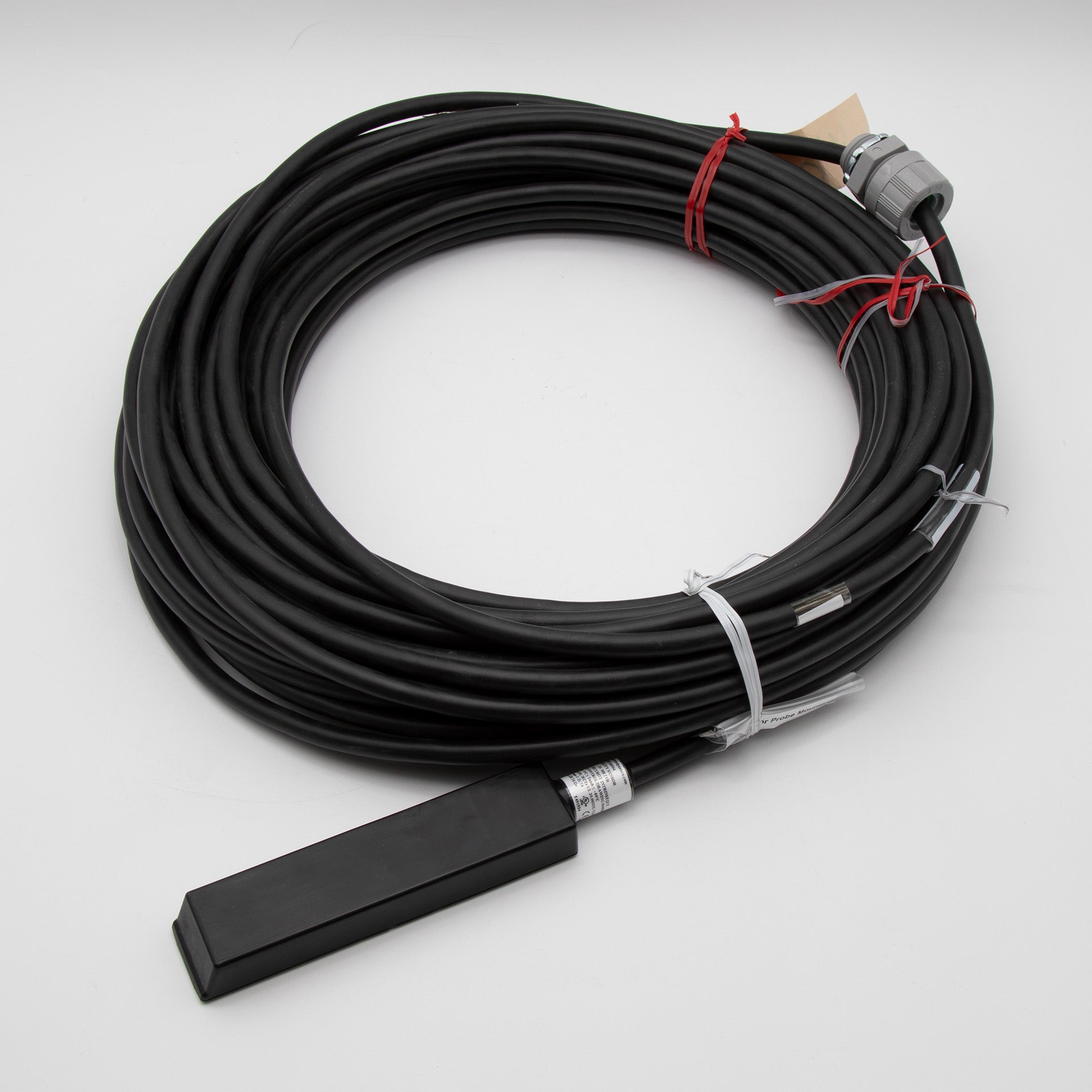 A black cable with a rectangular shaped sensor attached, positioned on a plain background.