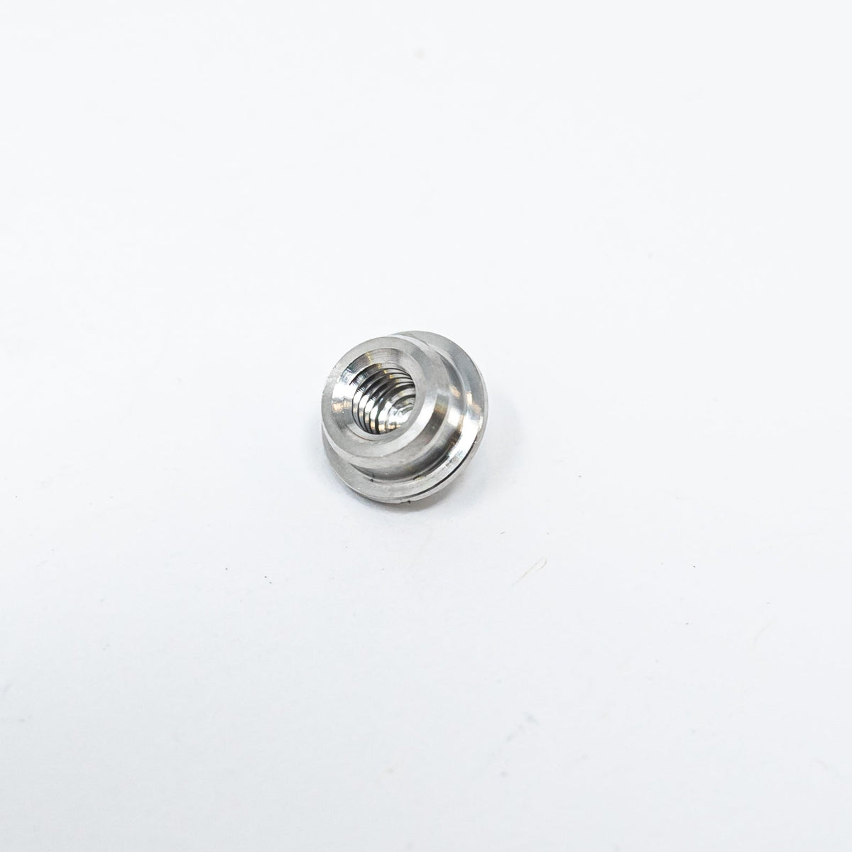 A small metal nut resting on a clean white surface, showcasing its shiny texture and circular shape.