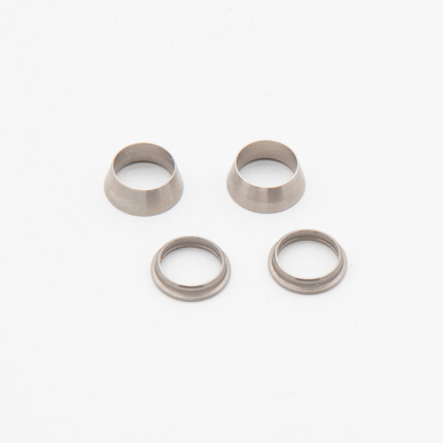 Four silver metal rings arranged on a smooth white surface, showcasing their reflective surfaces and circular design.