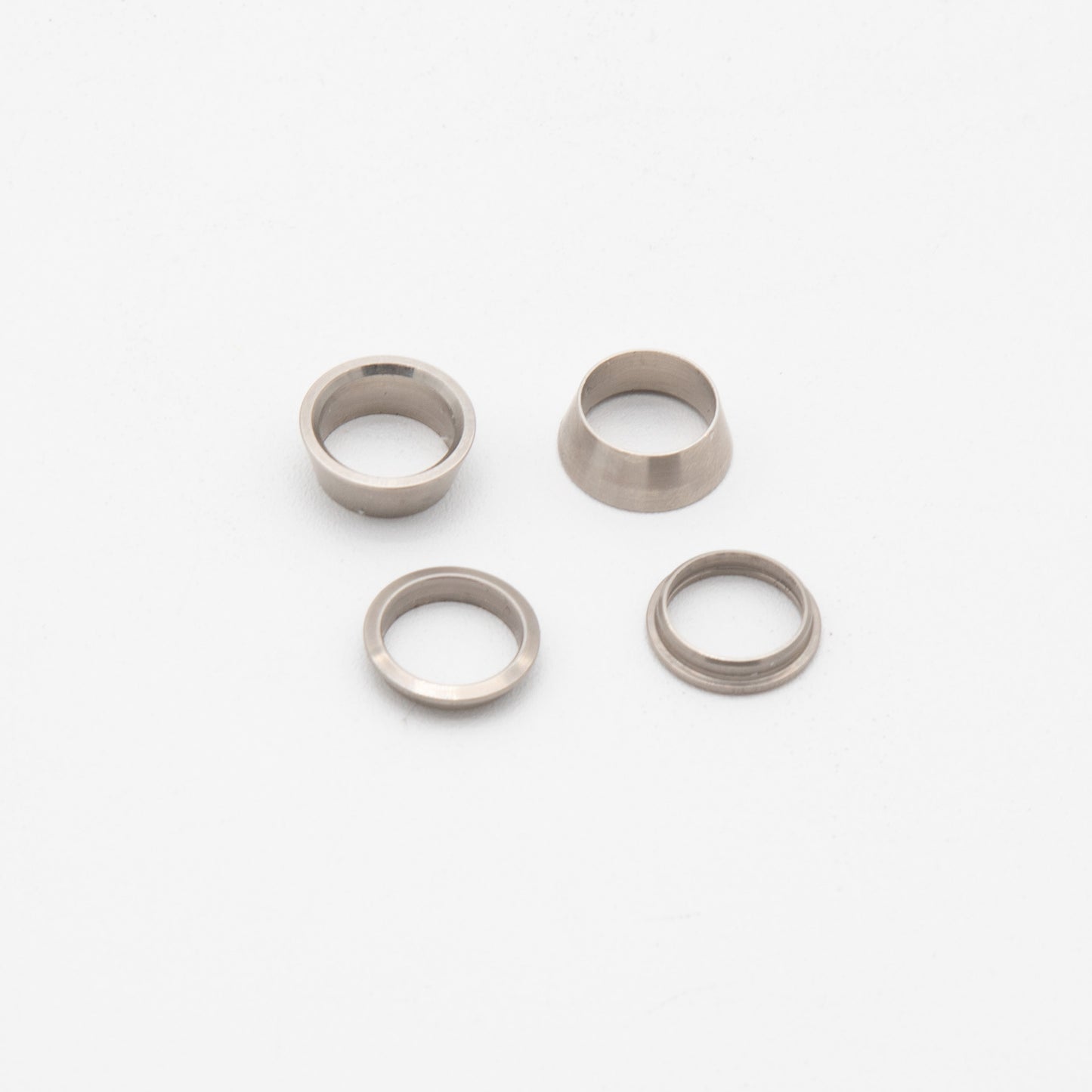 Four silver metal rings arranged on a smooth white surface, showcasing their reflective surfaces and circular design.