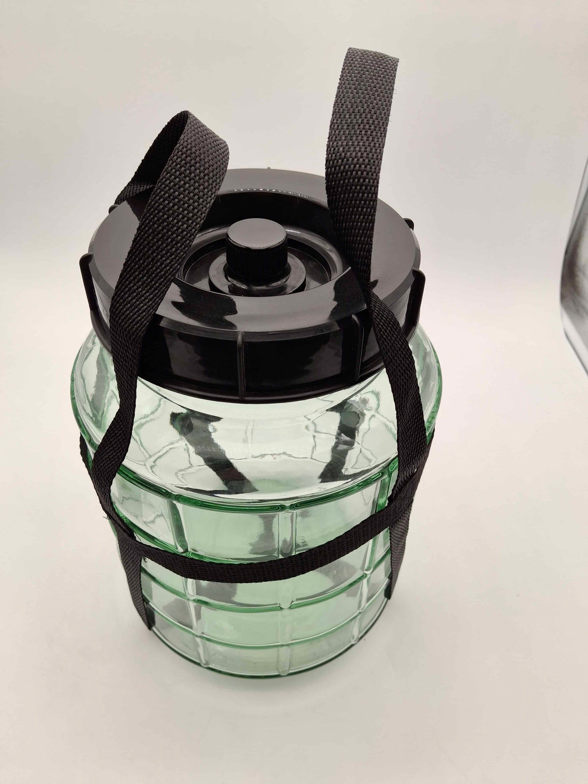 A clear ribbed glass jar with a black lid and black webbing carrying straps, photographed on a plain light background.