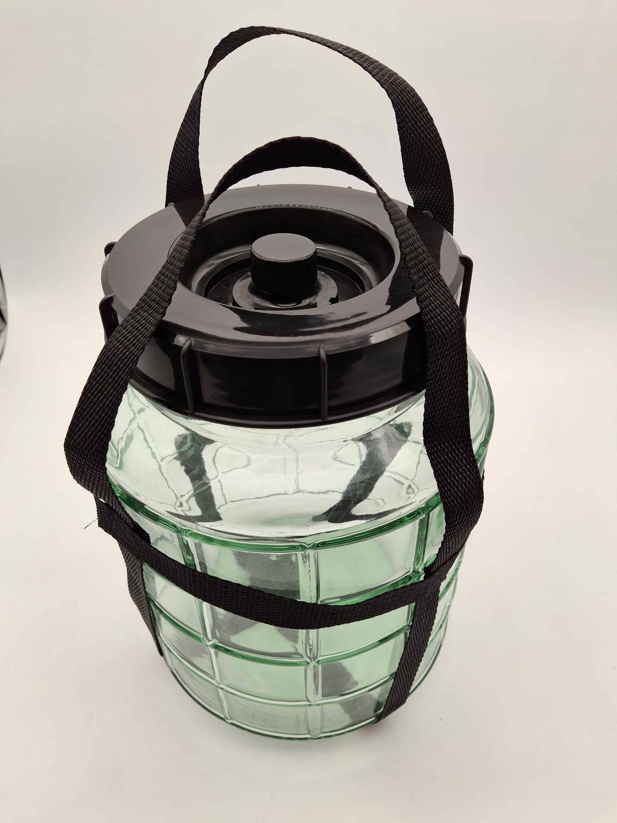A clear glass jar with a black screw-top lid and black carrying straps, photographed on a plain light background.