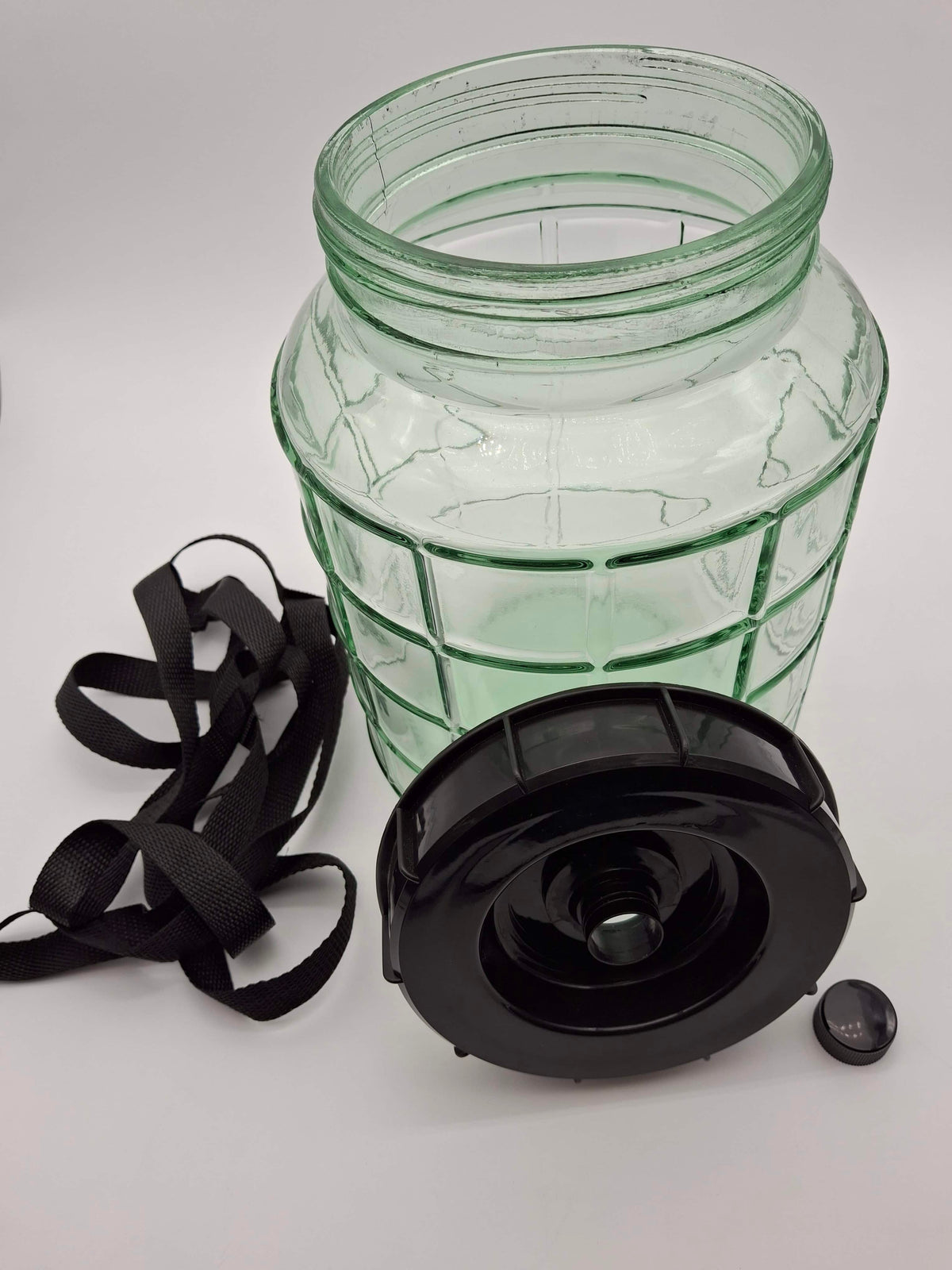 A clear ribbed glass jar with a green tint, shown with a black plastic lid and black carrying strap on a white background.