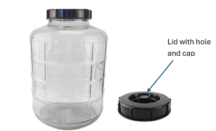 A clear cylindrical glass or plastic jar with a black screw cap shown next to a black lid with a hole and cap, labeled 'Lid with hole and cap' on a white background.