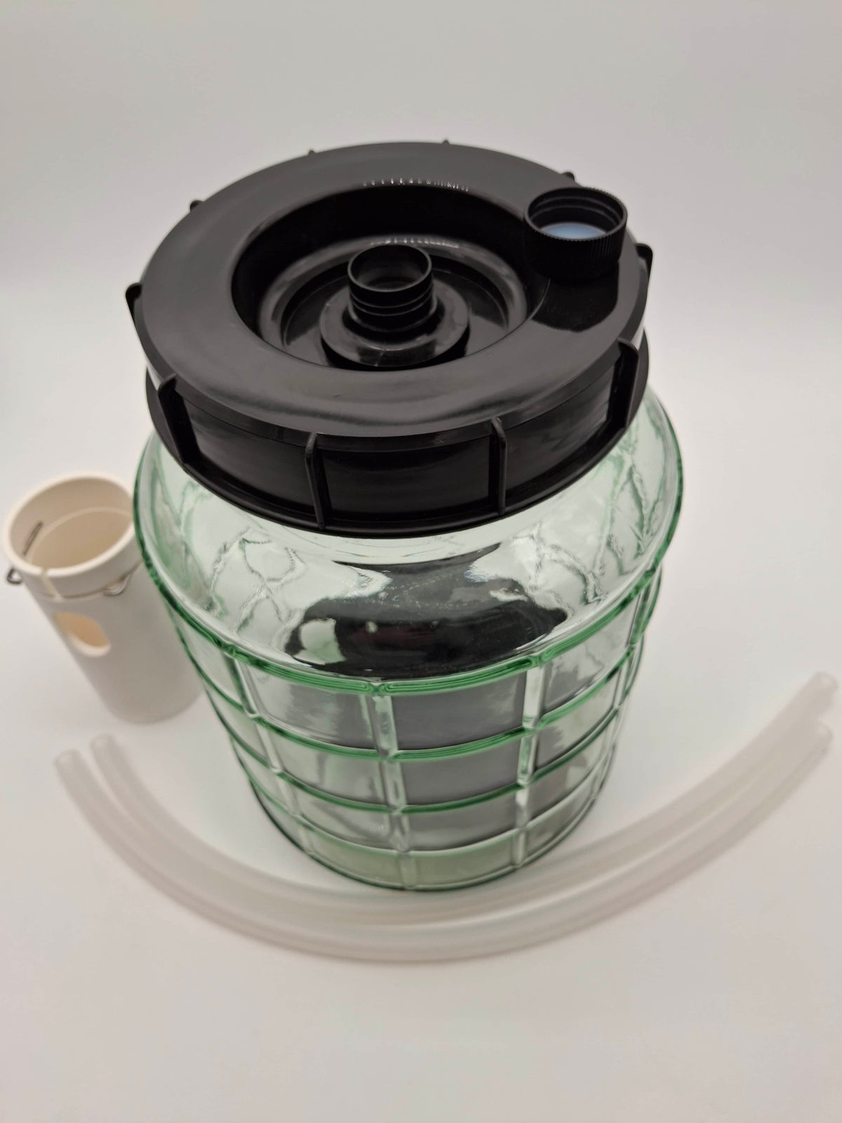 A clear glass jar with a black screw-on lid and a green grid-like pattern on the lower half, shown on a white background with a small white cup and translucent tubing nearby.