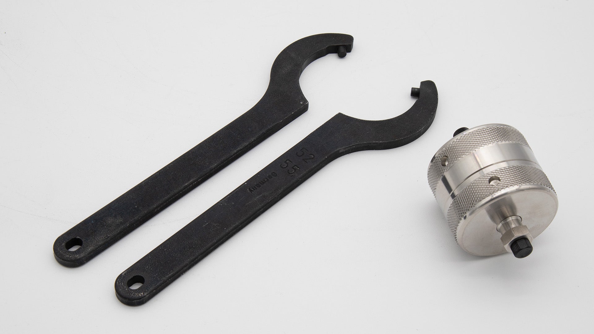 A pair of wrenches and a metal cylindrical shaped object arranged neatly on a clean white surface, showcasing their metallic finish.