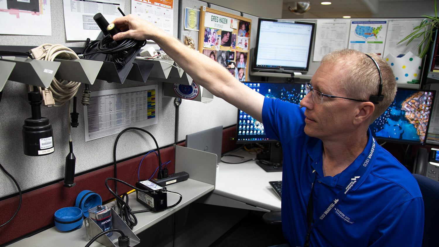 Person in a blue shirt working at a desk with computer monitors and equipment.