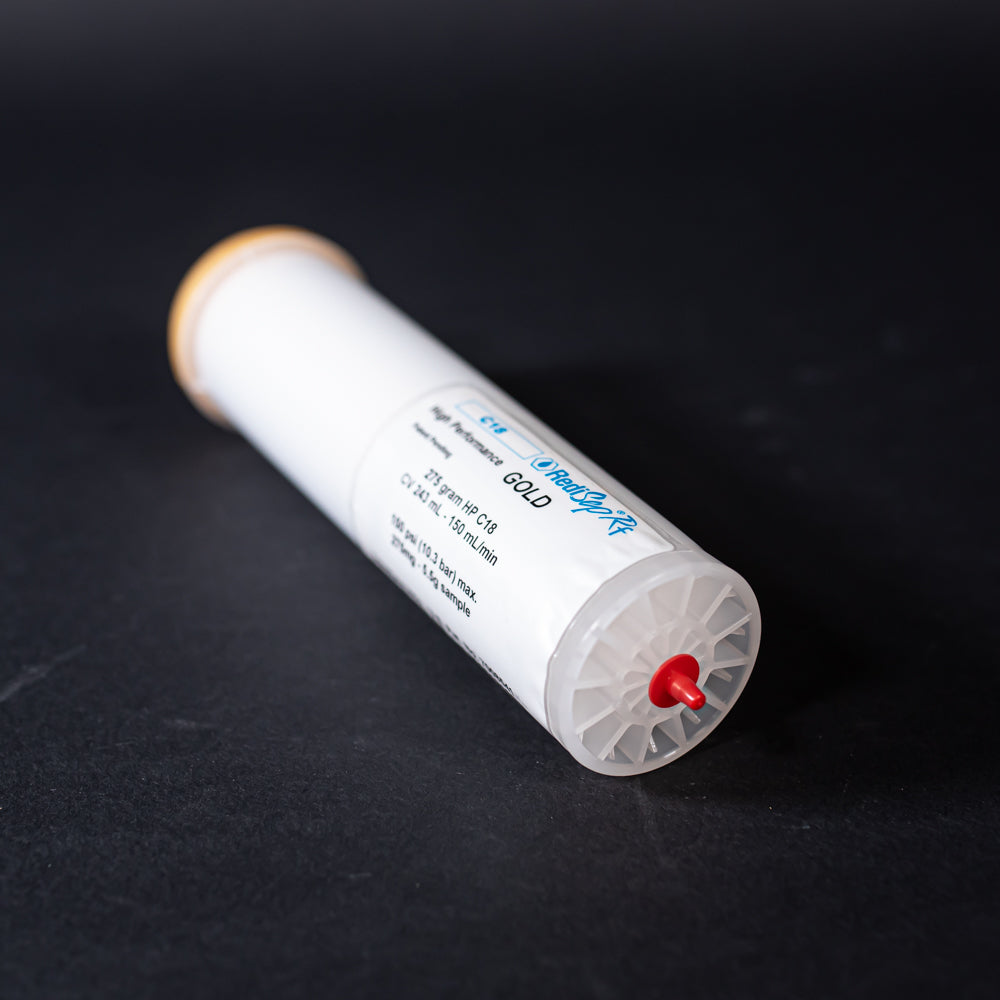 A small white tube with gold and red caps displayed on a black background, creating a striking visual contrast between the two elements.