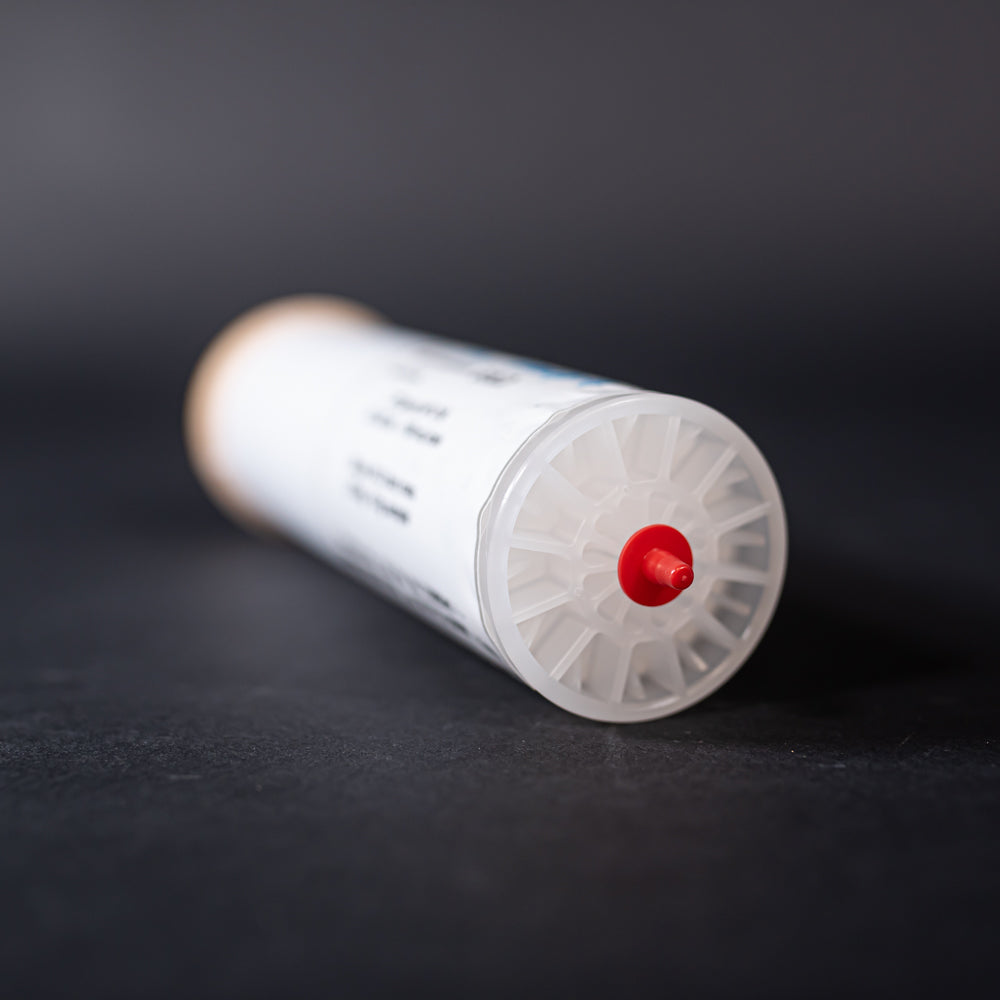 A small white tube with gold and red caps displayed on a black background, creating a striking visual contrast between the two elements.