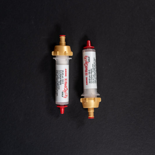 A set of small white tubes with gold and red caps displayed on a black background, creating a striking visual contrast between the two elements.